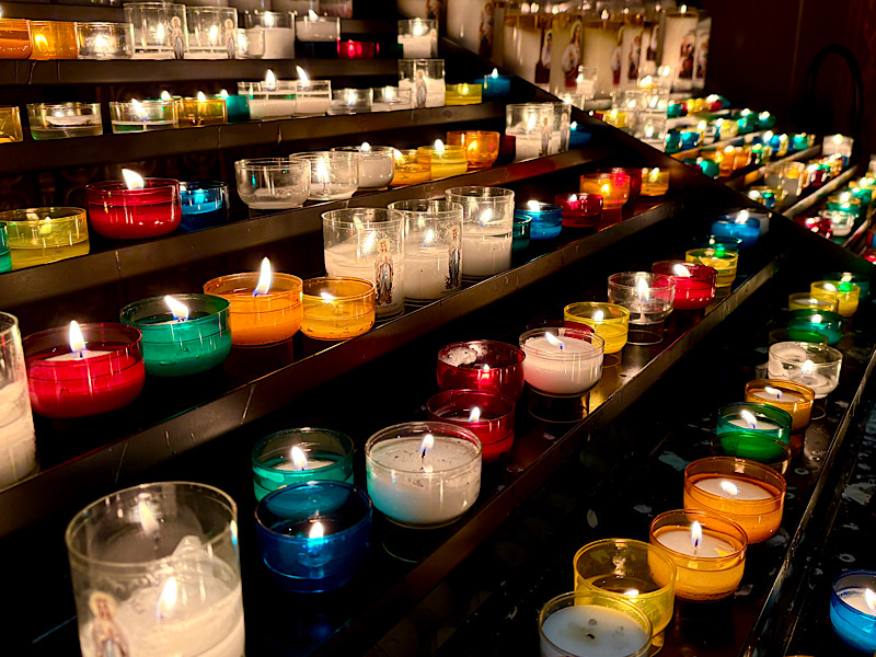 Enfilade de bougies multicolores allumées dans une église