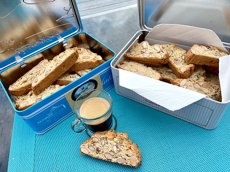 Deux boites pleines de biscuits italiens aux amandes derrière une tasse d’expresso et un biscuit prêt à être grignoté