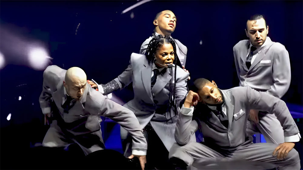 Janet Jackson en concert avec 4 danseurs en imperméable gris