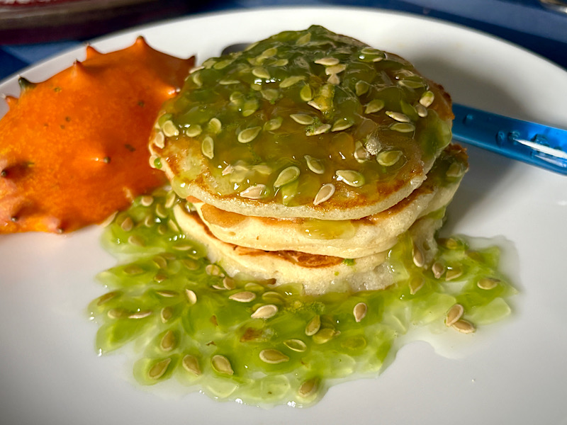 Dans une assiette, 3 pancakes recouvertes de jus et de graines de kiwano