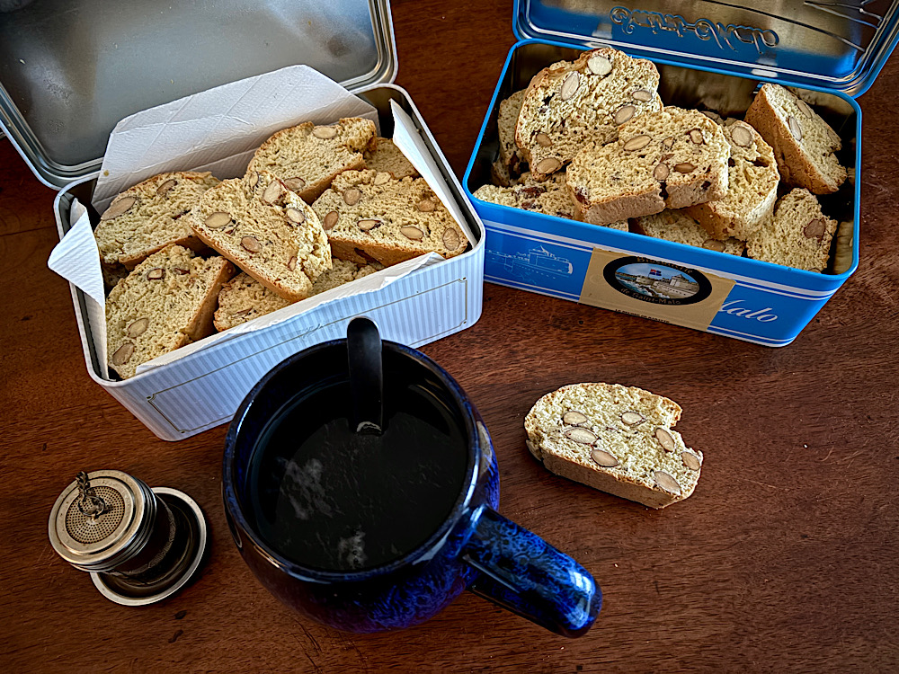 Deux boites de contuccini posées sur la table avec une grande tasse de thé et un boscuit prêt à être mangé