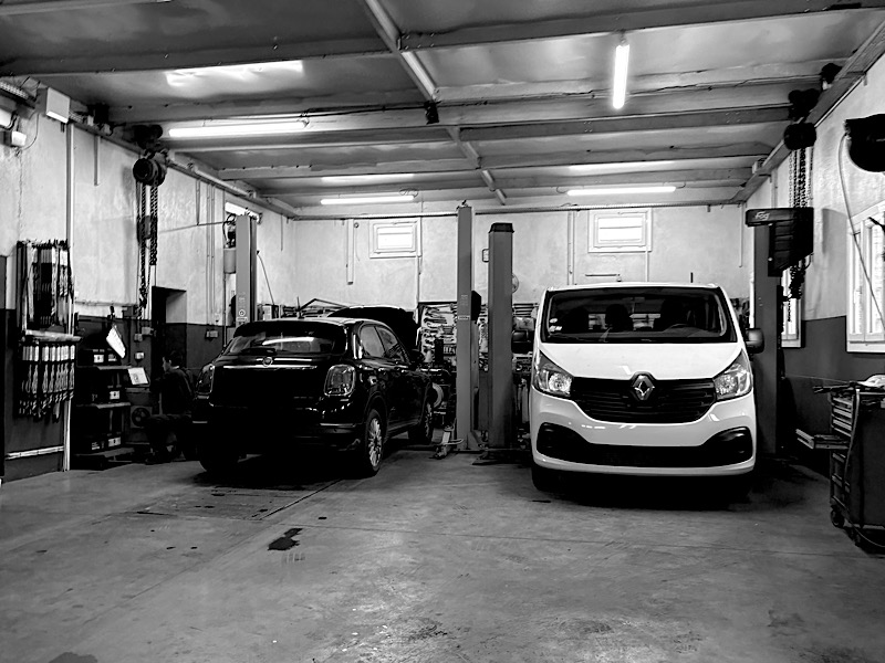 Photo noir et blanc de l’intérieur d’un garage, avec une voiture et une fourgonnette à l’intérieur et le garagiste à genoux sur le côté gauche